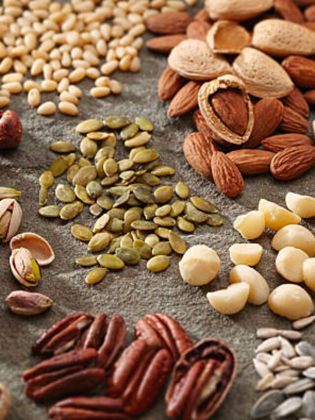 A variety of healthy and organic nuts and seeds in piles on a slate surface.